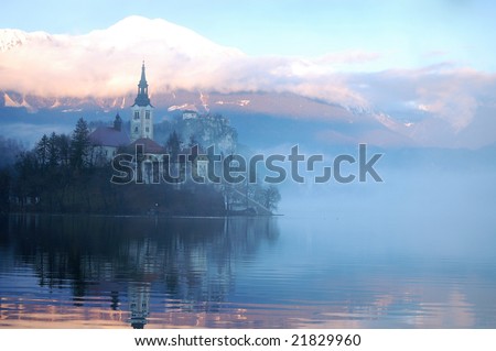 The Bled island church reflecting in the water with the snowy mountains and the Bled castle in the background