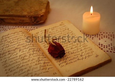 Dried red rose on an open old book by the candlelight