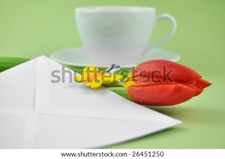 Red tulip and wooden butterfly on a white envelope with a cup of tea in the background