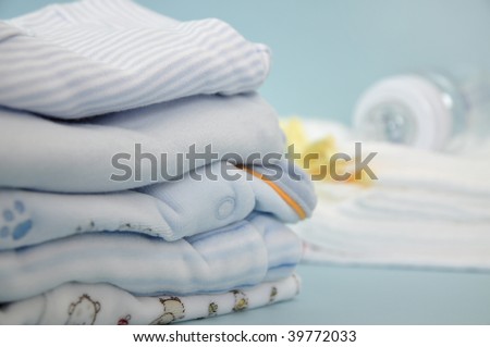 Pile of blue baby clothes and baby bottle on cotton diapers