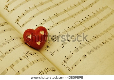 Red wooden heart on music sheet, toned sepia