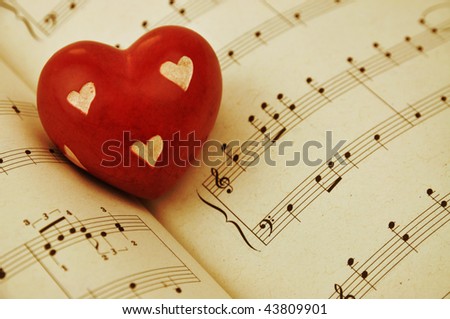 Red wooden heart on music sheet, toned sepia