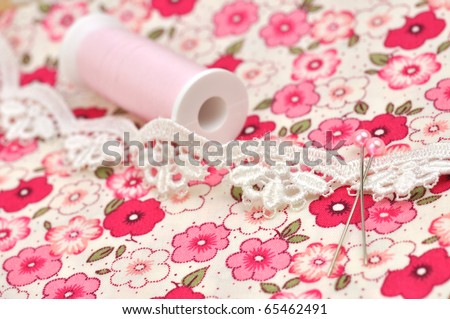 Spool, lace and straight pins on floral cloth