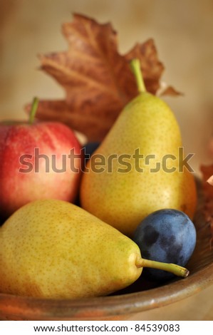 Ripe yellow pears, plum and red apple in a clay bowl