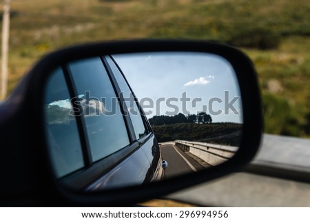 reflections in a mirror of a car driving by day