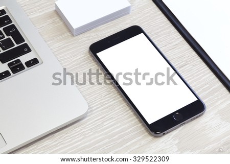 Laptop on working wooden table with smartphone, business card and blank for mock up