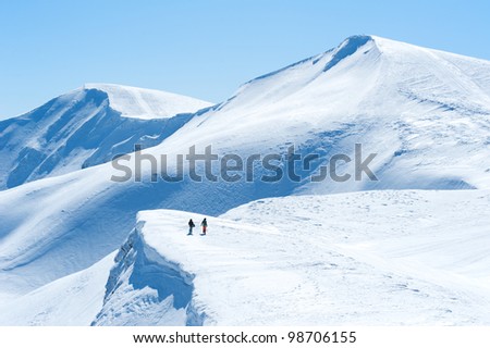 landscape of mountains and snowy peaks two people snowboarder or skier in the distance