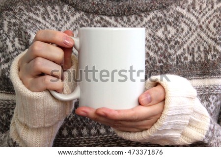 Girl in warm sweater is holding white mug in hands. Mockup for winter gifts design.