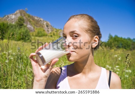 Girl drinks milk from a glass on a sunny day.