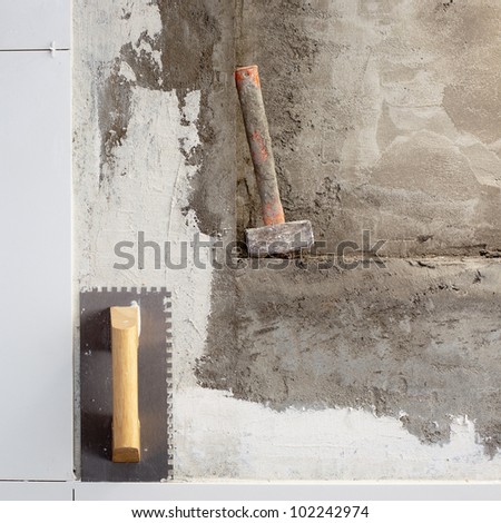 construction tools notched trowel and hammer on tiles mortar wall