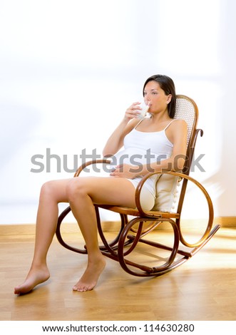 Beautiful pregnant woman drinking milk at home on rocker chair