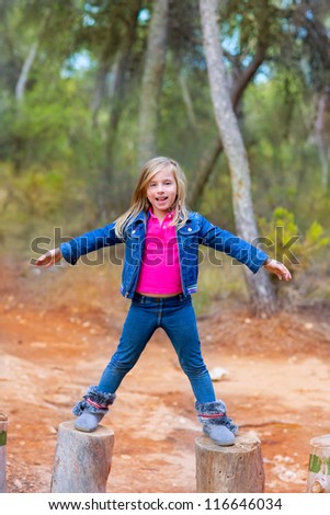 kid girl climbing tree trunks with open arms having fun in the pine forest