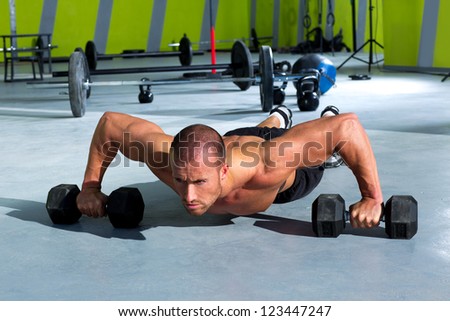 Gym man push-up strength pushup exercise with dumbbell in a workout