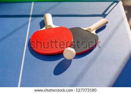 table tennis ping pong two paddles and white ball on blue board