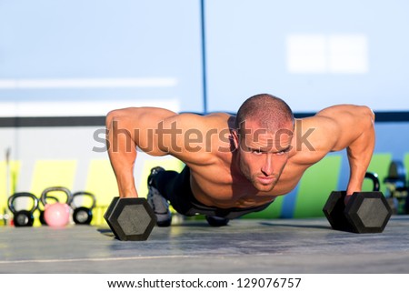 Gym man push-up strength pushup exercise with dumbbell in a fitness workout