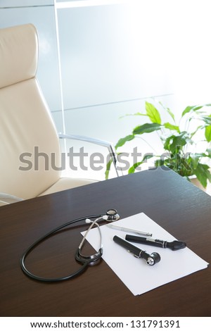 Doctor office table desk and beige chair with stethoscope otoscope and white paper
