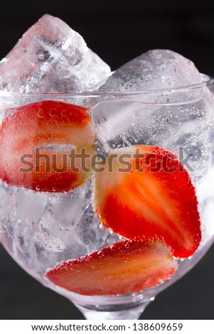 Gin tonic cocktail with strawberries ice macro closeup on black