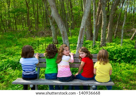 Children sister and friend girls sitting on park bench looking at forest and smiling