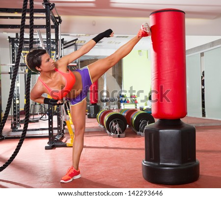 Crossfit fitness woman kick boxing with red punching bag at gym