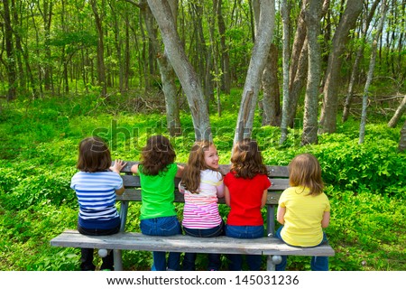 Children sister and friend girls sitting on park bench looking at forest and smiling