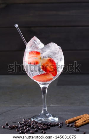 Gin tonic cocktail with strawberries ice cinnamon and juniper berries on black