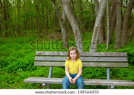 blond lonely children girl happy sitting on park bench on forest jungle