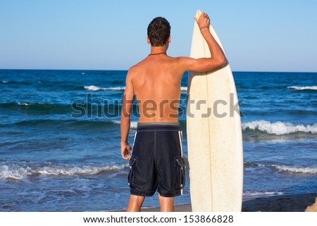 Boy surfer back rear view holding surfboard on blue beach