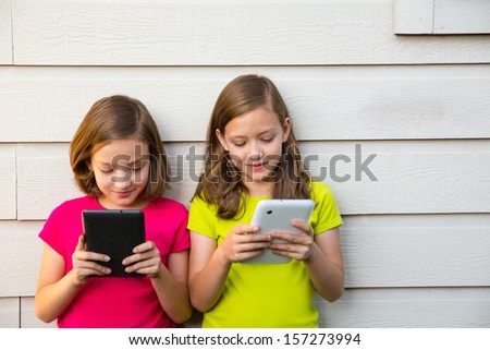Twin sister girls playing with tablet pc happy on white wall looking screen