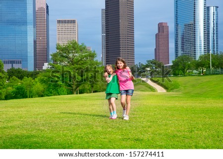 Two sister girls friends walking  in urban modern skyline on park lawn