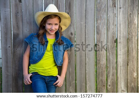 Children girl as kid cowboy girl cowgirl posing on wooden fence far west style