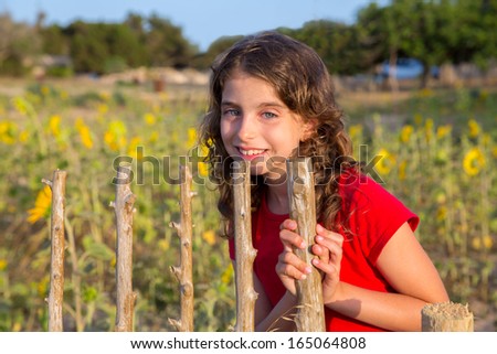 Smiling farmer girl with sunflowers field holding fence door in Mediterranean
