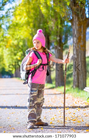 hiking kid girl with walking stick and backpack exploring autumn track and camouflage pants