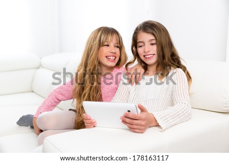 Children friends kid girls playing together with tablet pc on white sofa