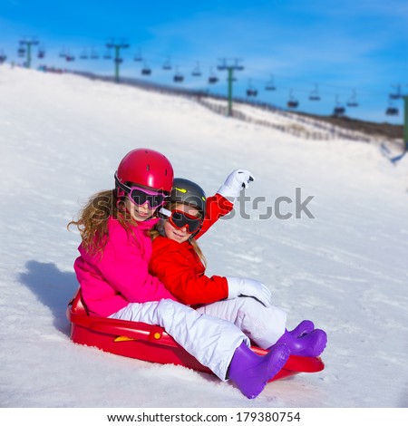Kid girls playing sled in winter snow with helmets and goggles [photo illustration]