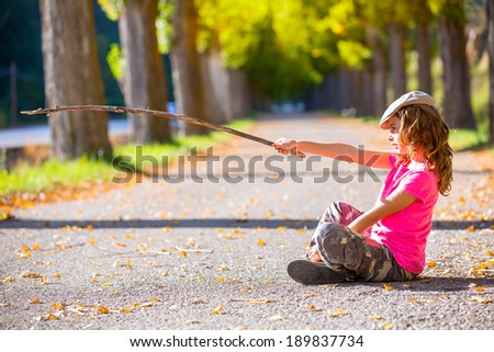 autumn kid girl with camouflage pants pointing with hiker branch stick