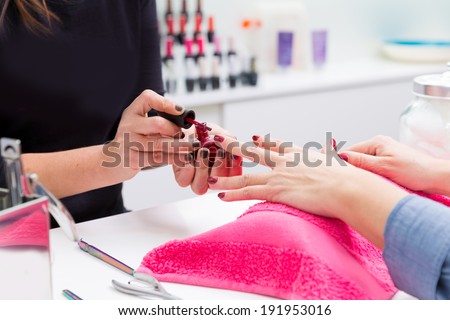 Nail saloon woman painting color nail polish in hands over pillow with pink towel