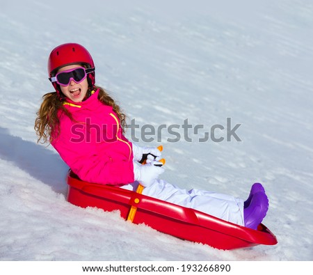 Kid girl playing sled in winter snow with helmet and goggles