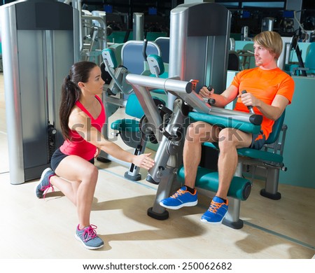 Gym seated leg curl machine exercise blond man and personal trainer woman