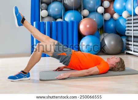 hip lift with leg extension blond man at gym workout with swiss ball background