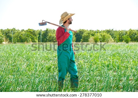 Farmer man with hoe looking at his orchard field with hat