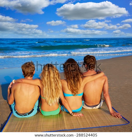 friends group couples sitting in beach sand rear view back looking to the sea