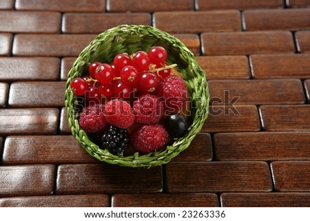 varied berries on a little green round basket over  dark wood
