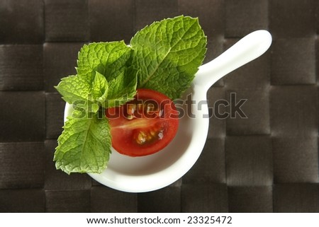 Half cherry tomato in a little dish over brown tablecloth and basil leaves around