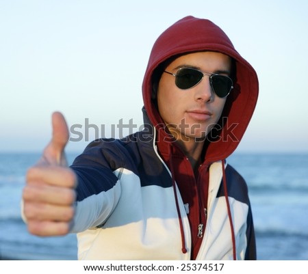 Grunge young man with hood and sunglasses at the beach