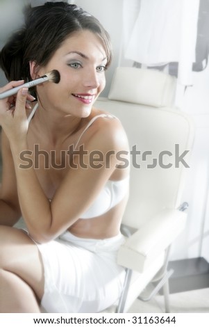 Beautiful woman with cosmetic brush on a makeup white chair in salon