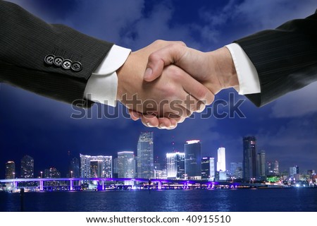 Businessman handshake in Miami downtown night cityscape [Photo Illustration]