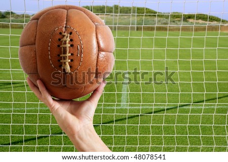 Football vintage ball in hand net soccer goal green grass background [Photo Illustration]