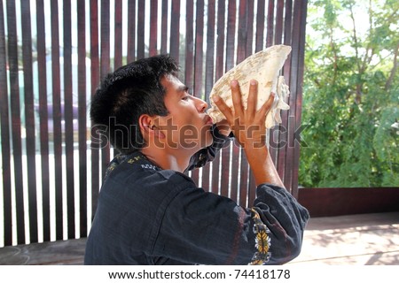 Mayan indian native man blowing seashell as horn in jungle Latin American