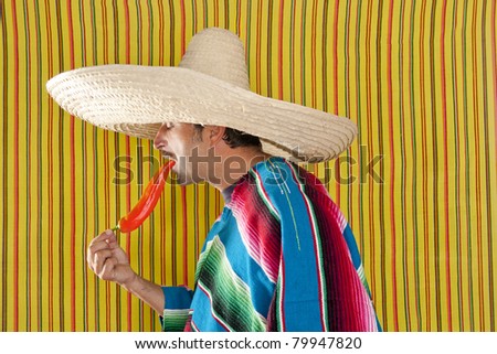 Mexican typical man eating chili hot pepper with poncho on yellow background