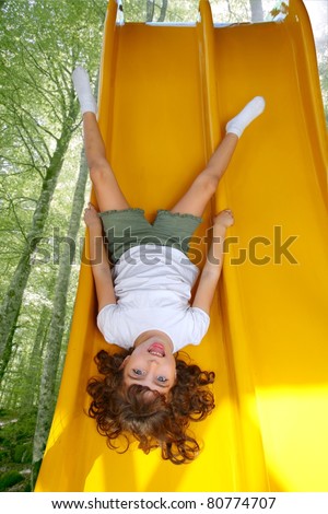 upside down little girl on playground slide laughing in forest tree park [Photo Illustration]